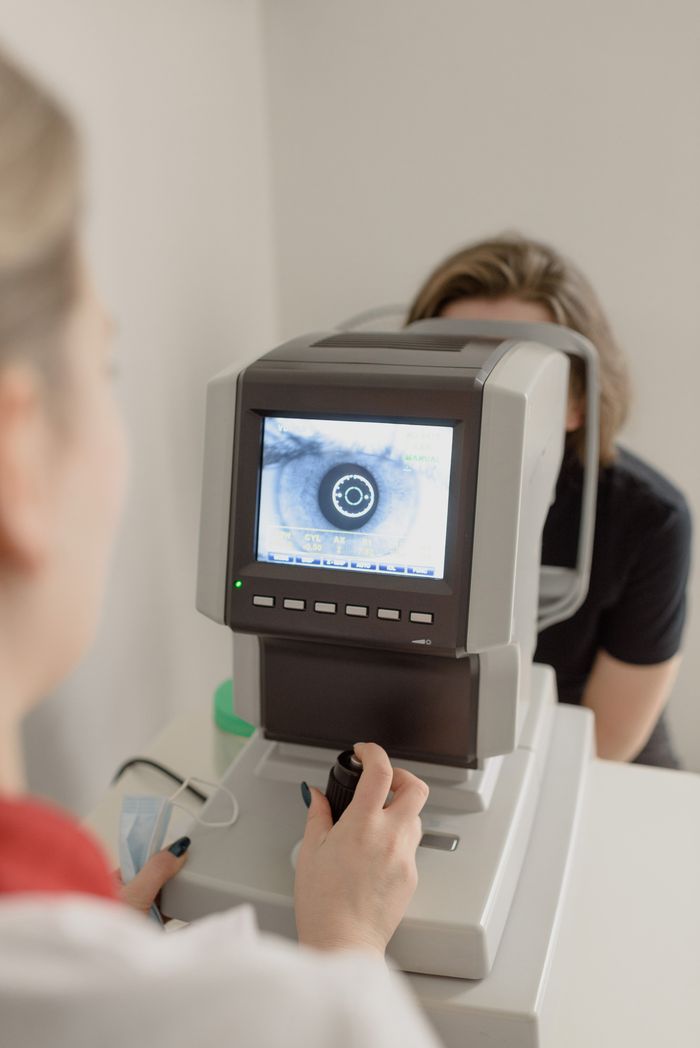 Crop anonymous oculist using vision screening device with eye illustration on monitor while examining eyesight of female patient in clinic